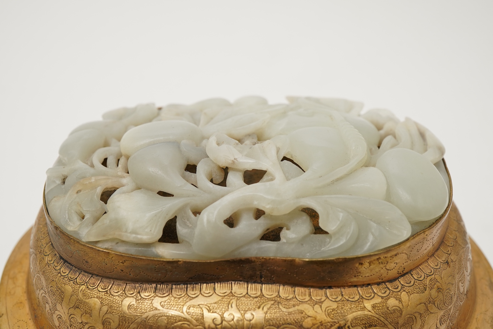 A Chinese pale celadon jade oval plaque, 17th/18th century, mounted on a late Qing gilt copper jar